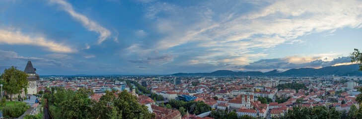 Fototapeta na wymiar Cityscape of Graz and the clock tower (Grazer Uhrturm), famous tourist attraction on Shlossberg hill, Graz, Styria region, Austria, at sunset. Dramatic sky, panoramic view