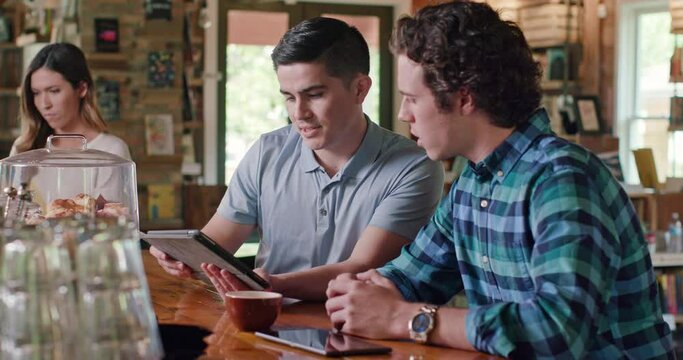 Young men sitting at counter in cafe bookstore looking at tablet 