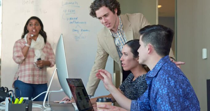 Co-Workers talking at computer in office while woman is working on dry erase board with flowchart 