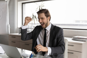Overjoyed businessman employee wearing suit looking at laptop screen, reading unexpected good news in business email, executive celebrating success, job promotion, reward or business achievement
