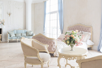 luxurious light interior in the Baroque style. A spacious room with a road chic beautiful furniture, a fireplace and flowers. plant stucco on the walls and light wood parquet