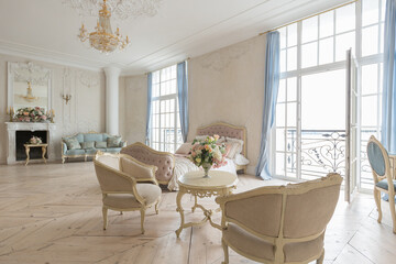 luxurious light interior in the Baroque style. A spacious room with a road chic beautiful furniture, a fireplace and flowers. plant stucco on the walls and light wood parquet