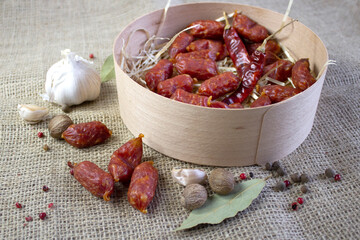 Appetizing sausages with garlic and spices in wood basket on rough linen background, flatlay, close up