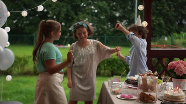 Cute teenagers dance at the birthday party around the set table. Schoolchildren have fun, happy childhood