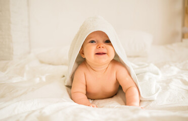 Fototapeta na wymiar a cheerful baby girl lies in a white bath towel on a blanket on the bed