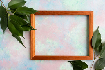 Wooden frame on a pastel background and branches with green leaves with space for text. Layout for postcard, banner, poster, invitation.