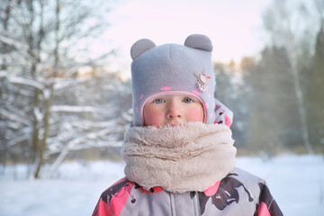 Closeup portrait of cute youg girl in winter forest. Warm clothes for the winter season.