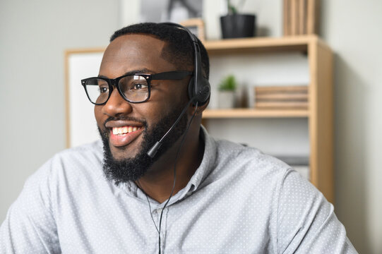 Young and handsome African-American employee wearing glasses, headphones with a microphone, talking to customers, communicating, and providing customer service on a helpline at the call center