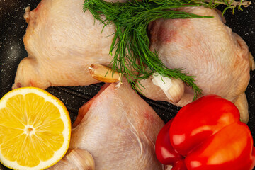 Raw chicken thighs laying in grill pan with lemon, bell pepper, greens and garlic . Top view close-up