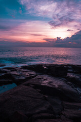 Krajobraz wybrzeża ze skałami nad oceanem z falami na tle pomarańczowego zachodzącego słońca. Piękne tropikalne tło.
