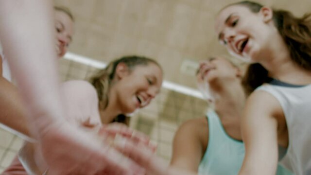 Low angle shot of happy, excited young volleyball team of girls putting hands together before start the game. Team spirit, cheering, support and sport theme. 