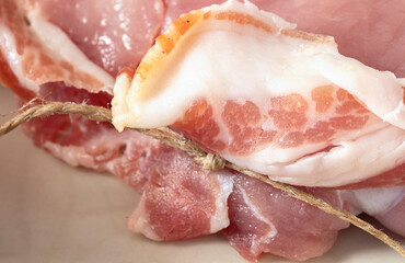 A slice of pancetta tied with a twine around a pork steak.