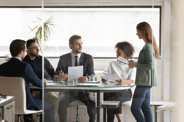 Businesswoman presenting financial project statistics to diverse colleagues at corporate briefing, standing in boardroom, discussing strategy with executive, business partners group negotiation