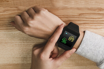 Woman measuring oxygen level with smartwatch at wooden table, top view