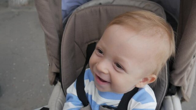 Little and funny boy sitting in the pram and waiting for mom. Baby in stroller on a walk in park. Adorable little boy in pushchair.