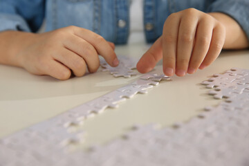 Fototapeta premium Little girl playing with puzzles at table, closeup