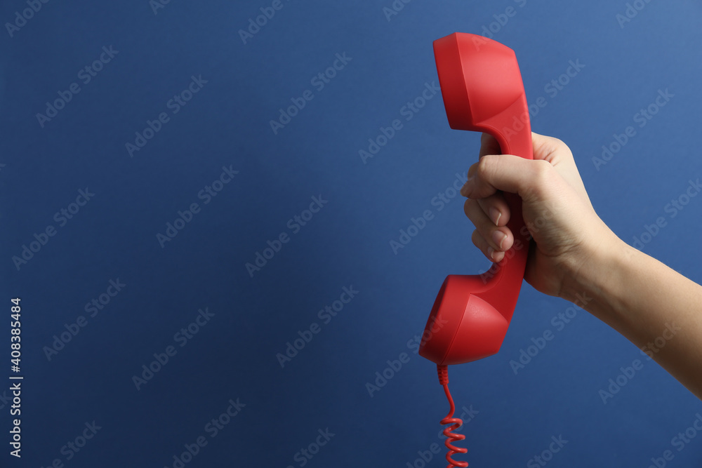 Wall mural Closeup view of woman holding red corded telephone handset on blue background, space for text. Hotline concept