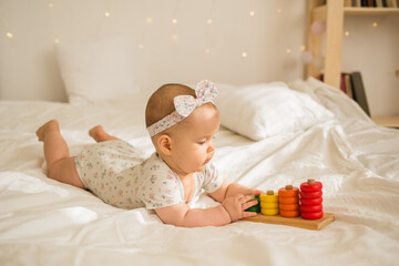a baby girl in a colorful bodysuit and headband plays with an educational toy on a white blanket on...