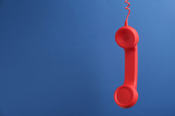 Red corded telephone handset hanging on blue background, space for text. Hotline concept