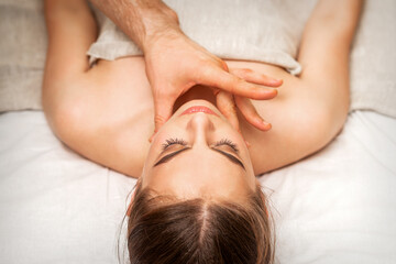 Fototapeta na wymiar Chin or neck massage of a young woman by the hand of a male massage therapist in a spa salon