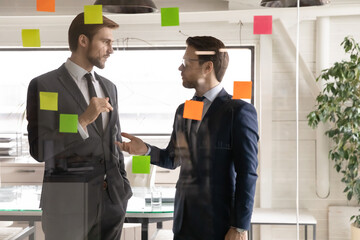Colleagues discussing corporate project strategy or marketing plan, standing near glass wall with...