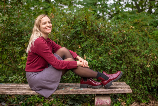 Smiling blond woman sitting on bench by plants in park during autumn