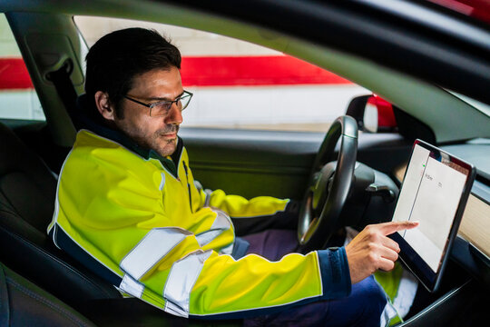 Male technician in uniform programming on digital tablet in car
