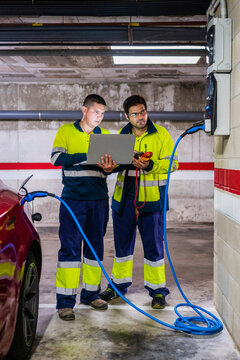 Male programmer discussing with colleague over laptop while charging electric car