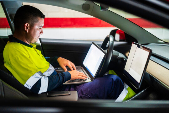 Male technician programming on laptop while sitting in electric car