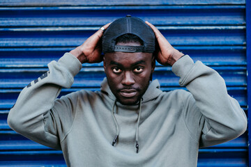 Confident young man wearing cap against blue corrugated wall