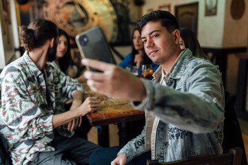 Young man taking selfie with friends through mobile phone at restaurant