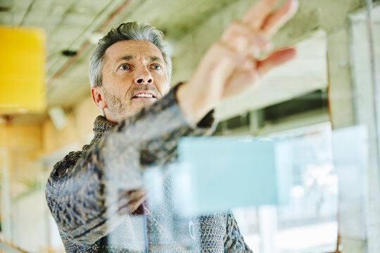Businessman planning while standing by glass wall at office