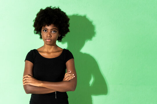 Young woman with arms crossed standing against green background