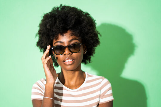 Woman adjusting sunglasses while standing against green background