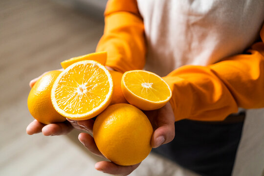 Woman holding orange and slice of orange in hand while standing at home