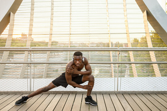 Confident sportsman doing stretching exercise on bridge