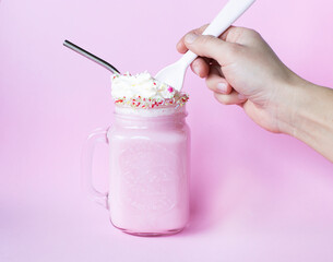 Hand taking cream from pink milkshake with cream and sprinkles