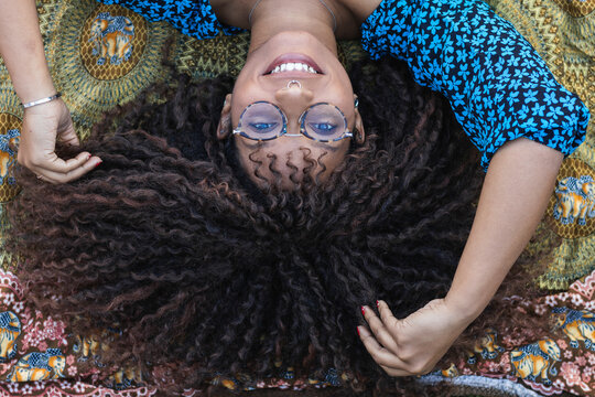 Smiling afro woman with hand in hair lying on blanket at public park