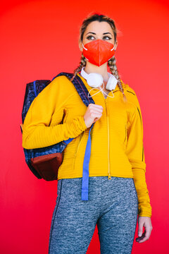 Athlete with face mask and backpack looking away while standing against red wall