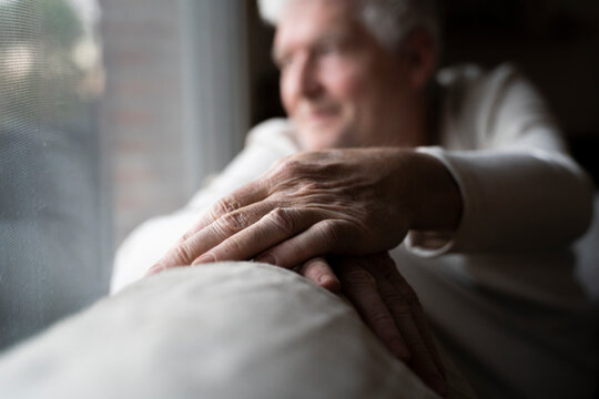 Senior man looking through window while sitting on sofa at home