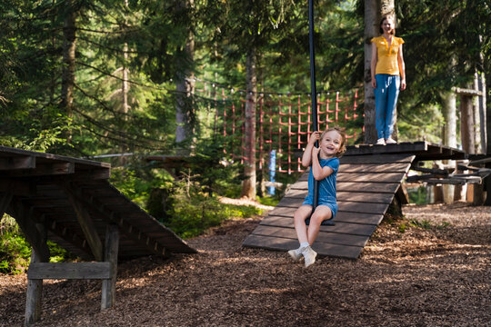 Little girl riding forest zip line with mother standing in background