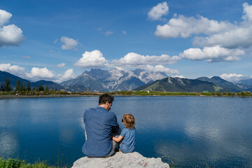 Fototapeta na wymiar Father and little daughter sitting together on top of lakeshore boulder