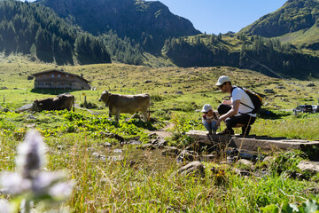 Father and daughter crouching over alpine stream during springtime hike