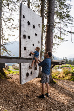 Father assisting little daughter trying to climb on top of small forest climbing wall
