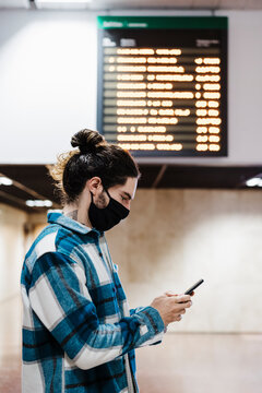 Man wearing protective face mask using mobile phone while standing at subway station