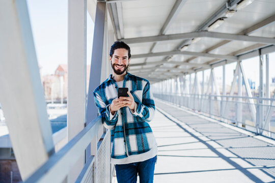 Smiling man using mobile phone while standing on bridge