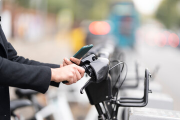 Man using smart phone for unlocking electric sharing bicycle in city