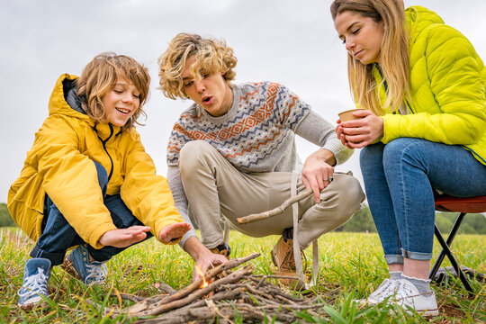 Three siblings starting campfire in grassy field