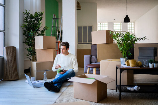 Young man with leafy salad looking at laptop in new home