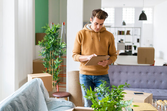 Young man checking list while moving in new loft apartment